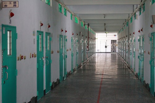The spacious and well-lit dormitory corridor is lined with multi-occupant rooms on both sides, each capable of accommodating 3 to 12 inmates. Above each room is a signal light, and inside each room is a call button. When an inmate presses the button, on-duty staff will promptly respond to check on the situation. Ceiling fans are installed along the corridor, and windows and exhaust fans are located at both ends of the corridor to ensure proper air circulation. Outside each room door, there is a nameplate displaying the names and bed positions of the inmates inside.